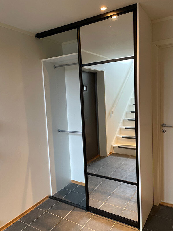Komplett skyvedørsgarderobe bestående av skyvedører med klart speil og svarte profiler og sprosser, og garderobeinnredning tilpasset på mål