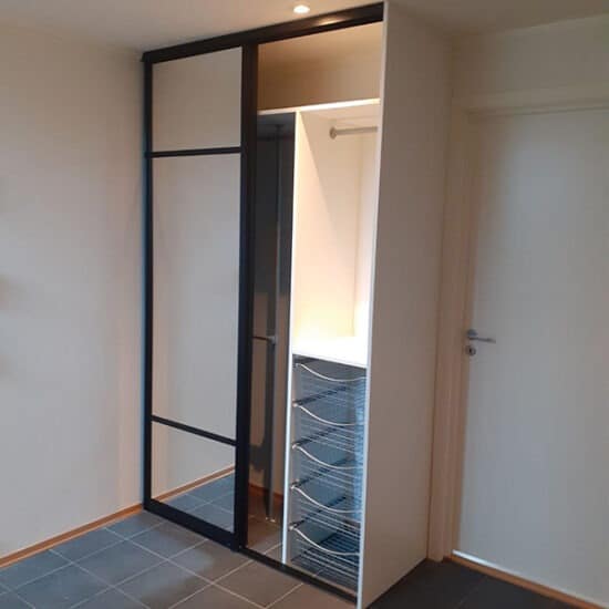 Komplett skyvedørsgarderobe bestående av skyvedører med klart speil og svarte profiler og sprosser, og garderobeinnredning tilpasset på mål